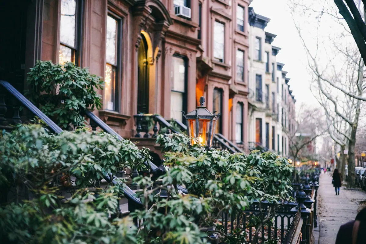 A row of brownstone stoops with a lantern glowing among the greenery