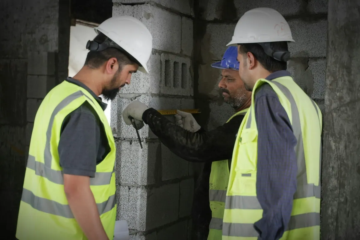 Two workers in hard hats assessing a block wall together