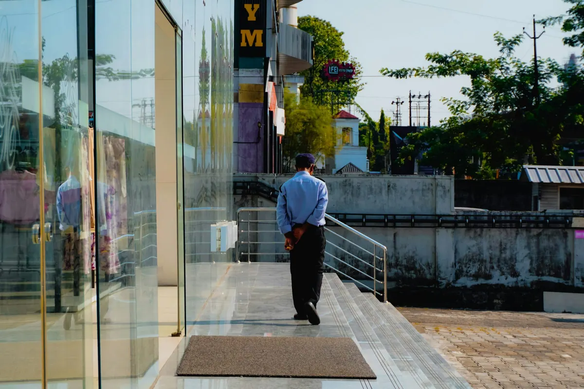 An officer in a pale blue shirt standing calmly at a glass building entrance
